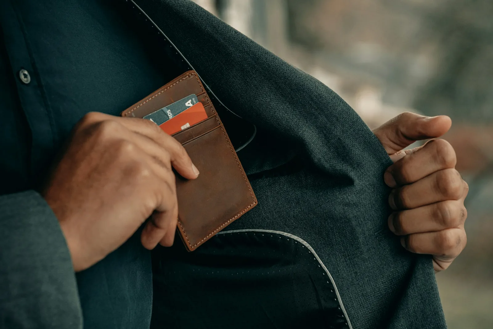 A slim leather wallet being placed in a jacket pocket